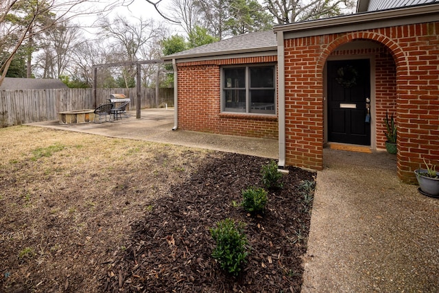 entrance to property featuring a patio area, brick siding, fence, and a lawn