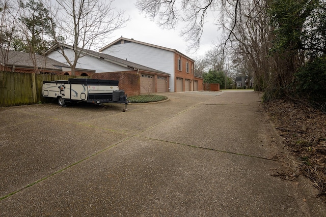 view of side of property with an attached garage, driveway, fence, and brick siding