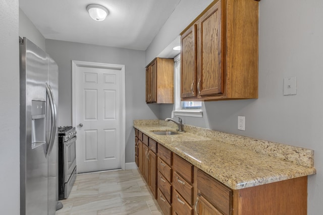 kitchen with light stone counters, appliances with stainless steel finishes, brown cabinetry, and a sink