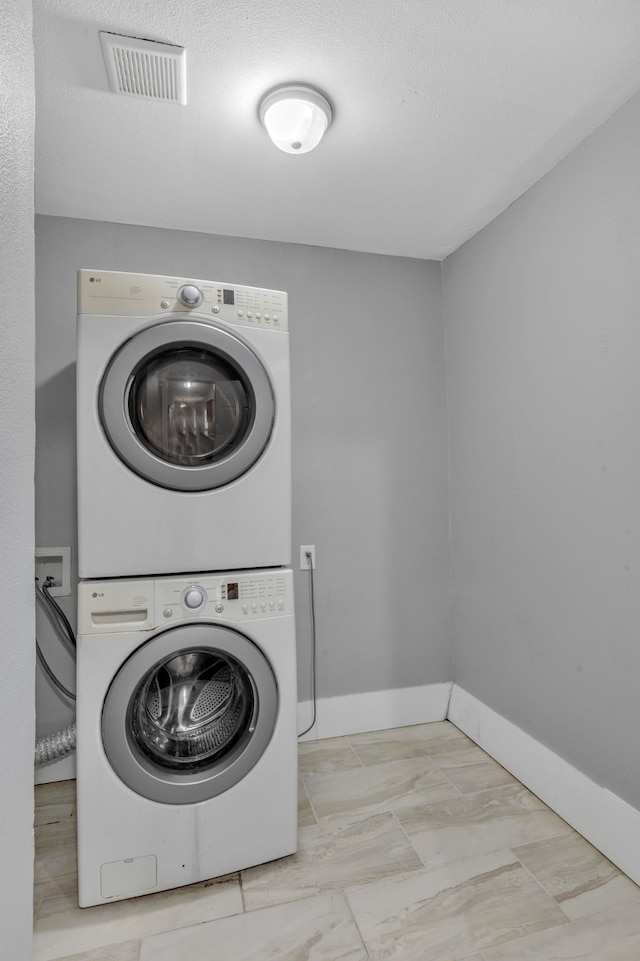 washroom with laundry area, baseboards, visible vents, stacked washer / drying machine, and a textured ceiling