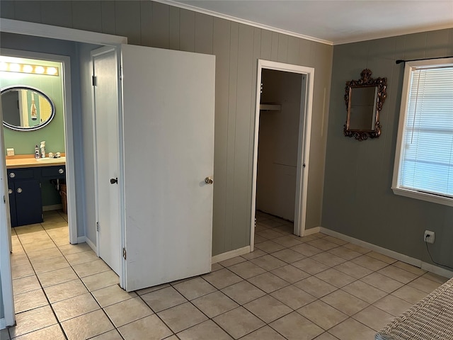 unfurnished bedroom featuring light tile patterned floors, baseboards, connected bathroom, crown molding, and a closet