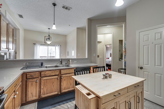 kitchen featuring butcher block countertops, visible vents, a sink, and decorative light fixtures