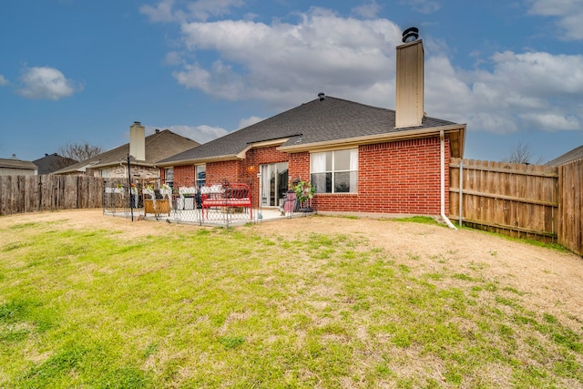 back of house featuring a patio, a fenced backyard, brick siding, a lawn, and a chimney