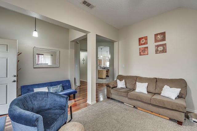 living room with a textured ceiling, wood finished floors, visible vents, baseboards, and vaulted ceiling