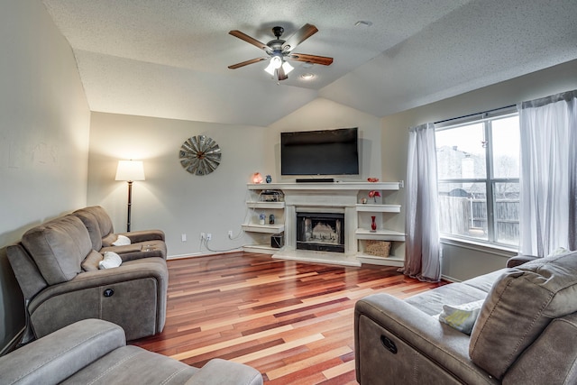 living room with a fireplace with raised hearth, a ceiling fan, lofted ceiling, wood finished floors, and a textured ceiling