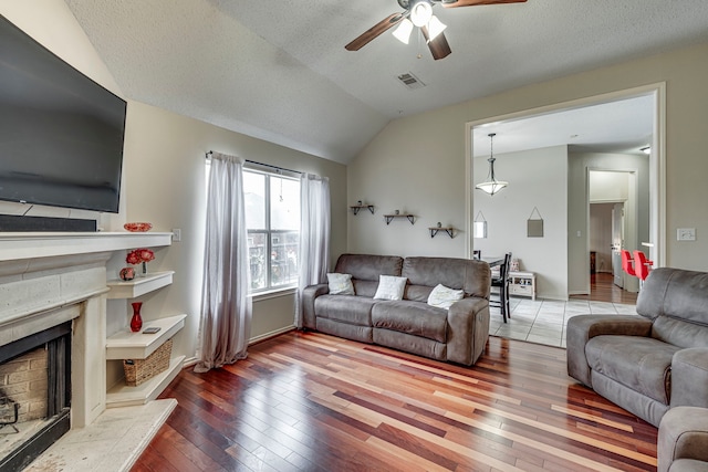 living room featuring visible vents, a high end fireplace, vaulted ceiling, a textured ceiling, and hardwood / wood-style flooring