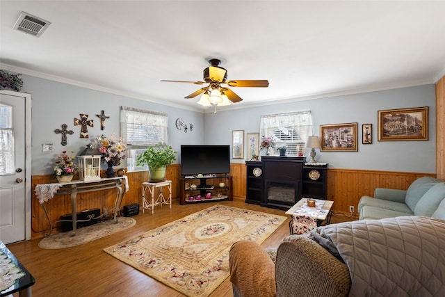 living room with a wainscoted wall, wood finished floors, visible vents, a ceiling fan, and ornamental molding