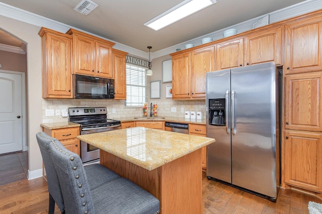 kitchen with light wood finished floors, visible vents, appliances with stainless steel finishes, ornamental molding, and a sink