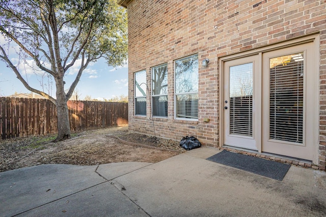 view of exterior entry with a patio area, fence, and brick siding