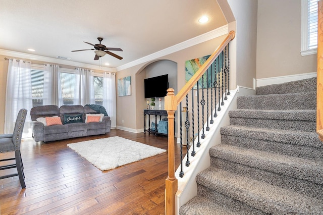 living area with arched walkways, a ceiling fan, stairway, hardwood / wood-style floors, and crown molding