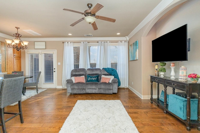 living area featuring baseboards, visible vents, wood finished floors, crown molding, and ceiling fan with notable chandelier