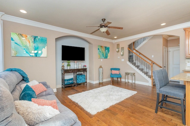 living room featuring arched walkways, light wood-style flooring, ornamental molding, baseboards, and stairs