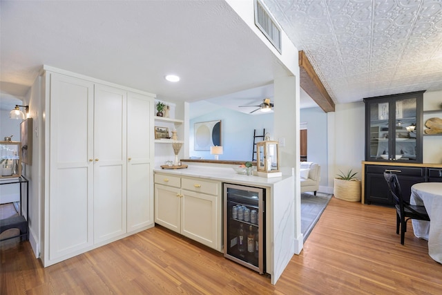 kitchen featuring visible vents, ceiling fan, beverage cooler, open floor plan, and light wood-type flooring