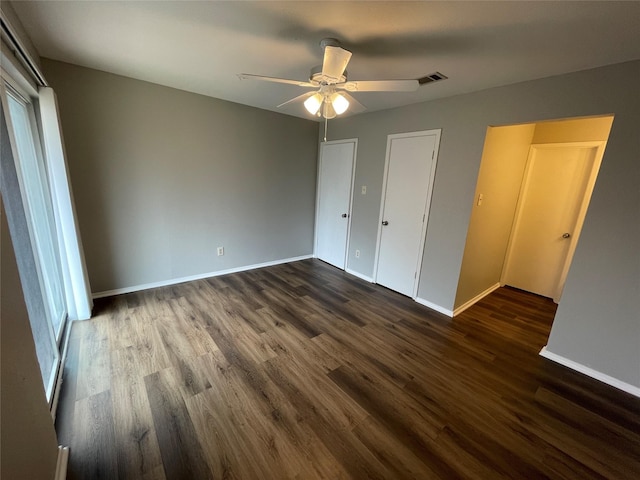 unfurnished bedroom with dark wood-type flooring, a ceiling fan, visible vents, and baseboards