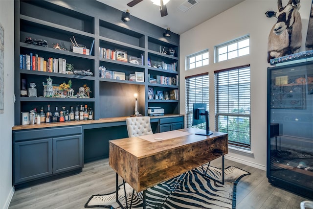 home office with built in features, light wood finished floors, visible vents, ceiling fan, and baseboards