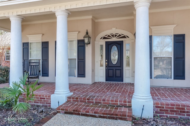 view of exterior entry featuring a porch and brick siding