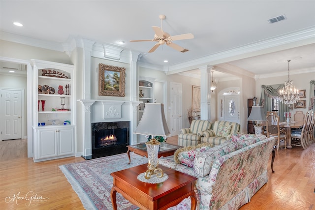 living room with ceiling fan with notable chandelier, a fireplace, visible vents, light wood-type flooring, and crown molding