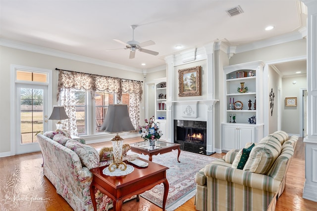 living room featuring wood finished floors, visible vents, a high end fireplace, built in features, and ornamental molding