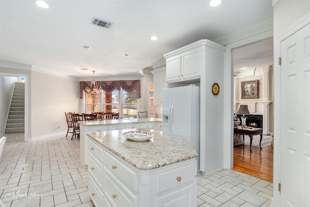 kitchen featuring a large fireplace, a peninsula, visible vents, a center island, and crown molding