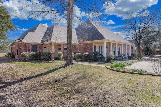 view of front of property featuring roof with shingles, a porch, a front lawn, and brick siding