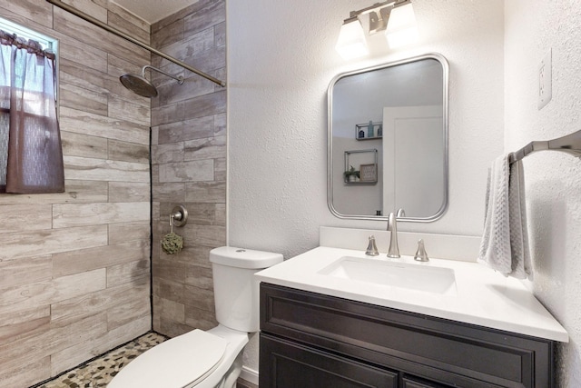 bathroom featuring a textured wall, a tile shower, vanity, and toilet