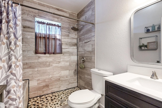 full bath with toilet, a textured wall, a tile shower, and vanity