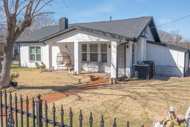 view of front of home featuring cooling unit, brick siding, fence, a front lawn, and a chimney