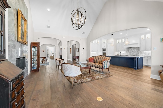 living room featuring visible vents, arched walkways, light wood-style flooring, an inviting chandelier, and high vaulted ceiling