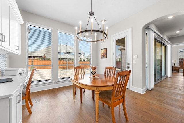 dining area featuring baseboards, arched walkways, an inviting chandelier, light wood-style floors, and recessed lighting