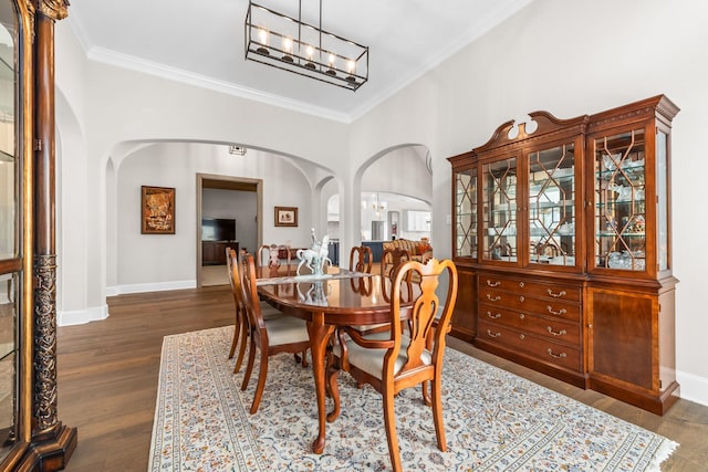 dining space with arched walkways, ornamental molding, dark wood finished floors, and a notable chandelier