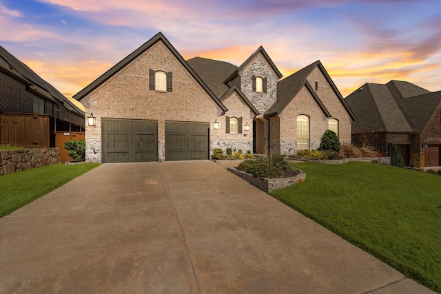 french provincial home featuring a garage, driveway, a front lawn, and brick siding