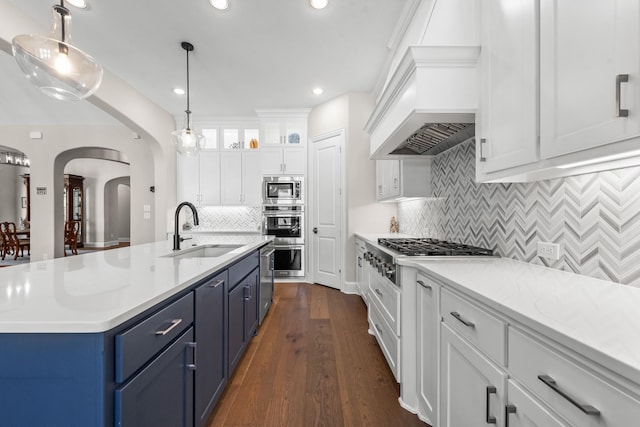 kitchen with arched walkways, a sink, white cabinetry, blue cabinetry, and appliances with stainless steel finishes