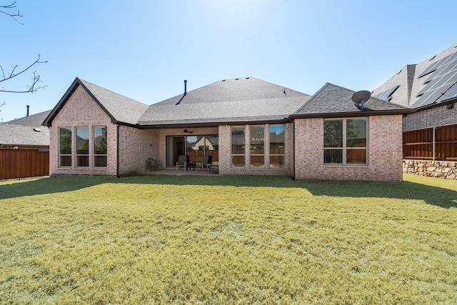 rear view of property with fence private yard, brick siding, and a yard