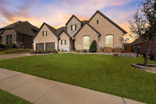 french country home with a garage, brick siding, a yard, and driveway