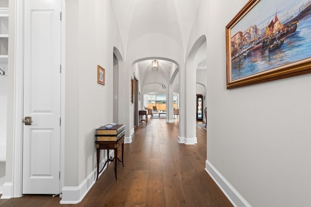 hall with dark wood-type flooring, arched walkways, and baseboards