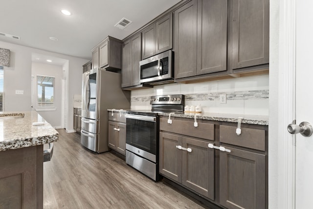 kitchen with stainless steel appliances, light wood-type flooring, visible vents, and light stone countertops