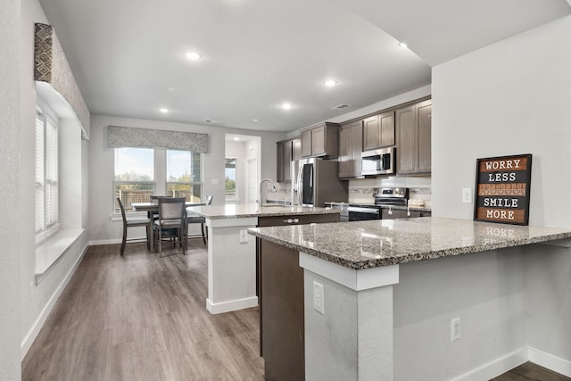 kitchen featuring a center island with sink, dark wood-style floors, appliances with stainless steel finishes, light stone counters, and a peninsula