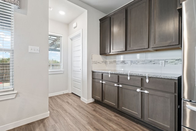 kitchen featuring dark brown cabinetry, baseboards, light wood-style flooring, light stone counters, and freestanding refrigerator