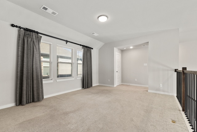 spare room with light colored carpet, visible vents, vaulted ceiling, and baseboards