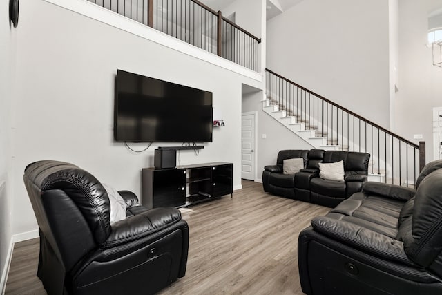 living area with stairs, baseboards, a high ceiling, and wood finished floors