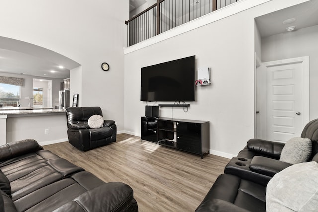 living room with arched walkways, baseboards, a towering ceiling, and light wood finished floors