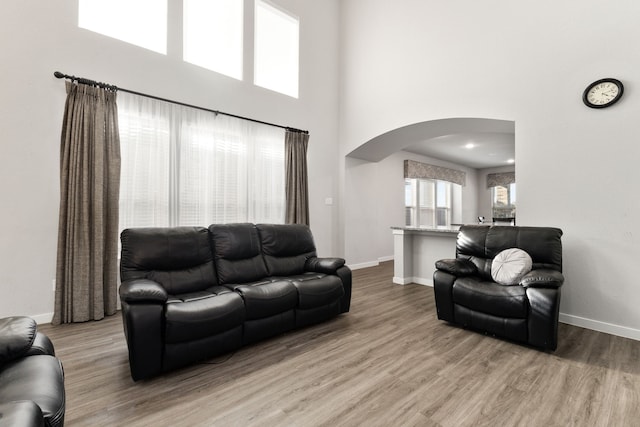 living room featuring a towering ceiling, baseboards, arched walkways, and wood finished floors