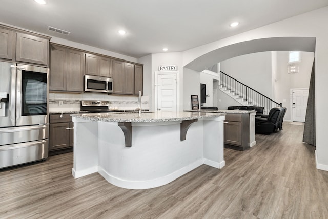 kitchen with arched walkways, a breakfast bar area, stainless steel appliances, visible vents, and light wood-type flooring