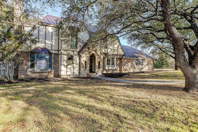 english style home with metal roof, brick siding, a standing seam roof, and a front yard