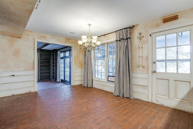 unfurnished dining area with brick floor, a wealth of natural light, and an inviting chandelier