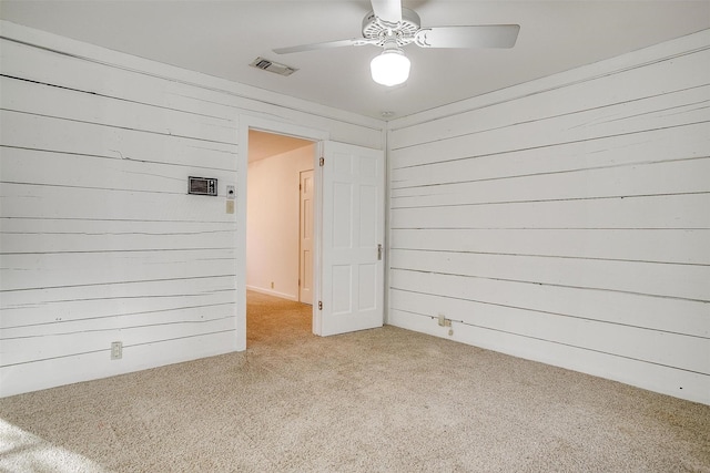 spare room featuring wood walls, visible vents, a ceiling fan, and light colored carpet