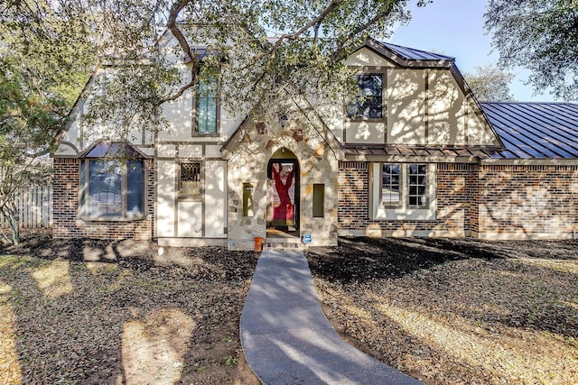 tudor home featuring metal roof, brick siding, and a standing seam roof