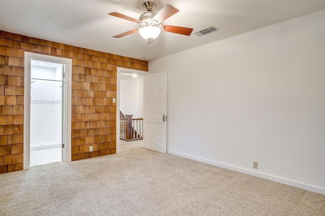 unfurnished bedroom with wooden walls, carpet flooring, a ceiling fan, visible vents, and baseboards