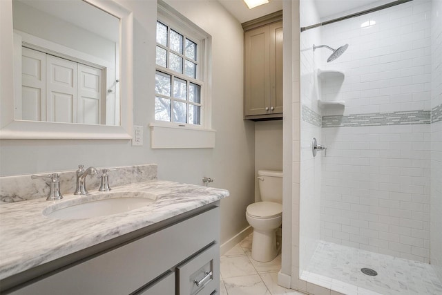 bathroom featuring marble finish floor, toilet, a tile shower, vanity, and baseboards