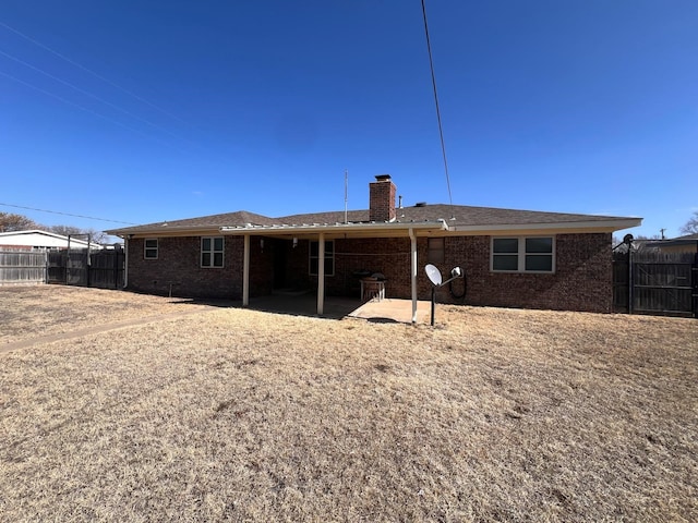 back of house featuring brick siding, fence, a chimney, and a patio